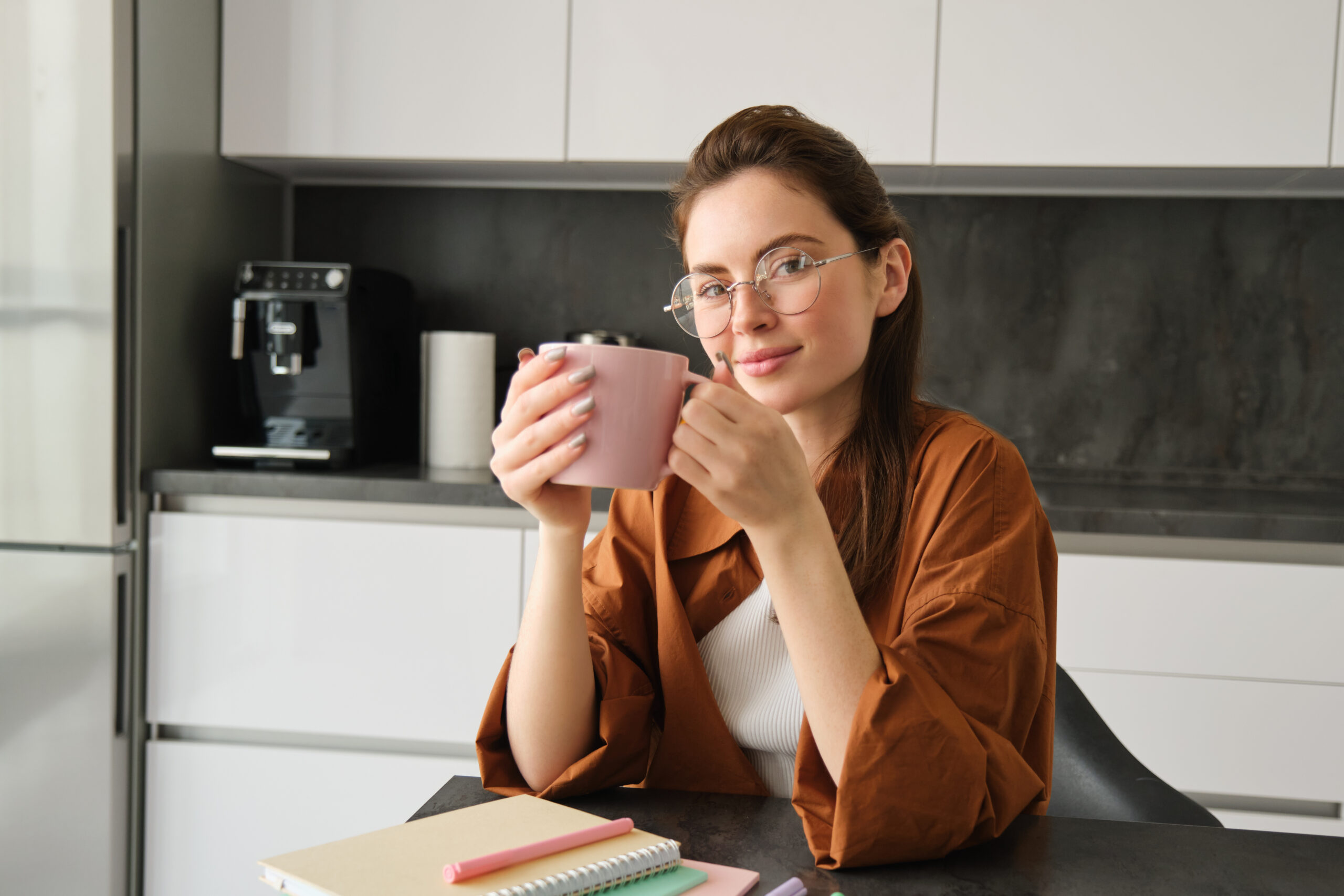 Portrait of beautiful brunette woman, sitting in kitchen, taking a break for cup of coffee. Girl drinks tea at home.